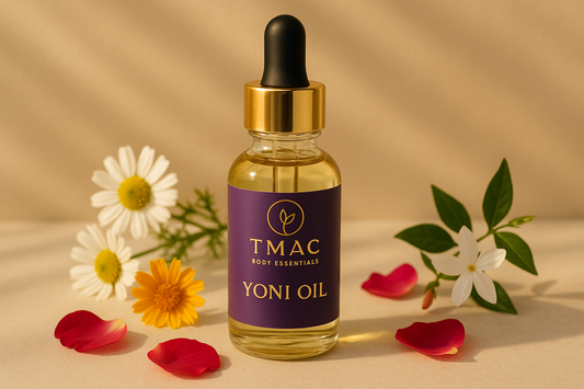 A high-resolution lifestyle product mockup of TMAC Body Essentials Yoni Oil. Show a sleek glass dropper bottle with a purple and gold label featuring the TMAC logo (circle with leaf accent) and the product name “Yoni Oil”. The label should feel elegant and organic. Place the bottle on a clean surface with natural lifestyle accents such as chamomile flowers, rose petals, calendula blossoms, and jasmine sprigs. Lighting should be soft, golden, and calming to reflect feminine wellness.